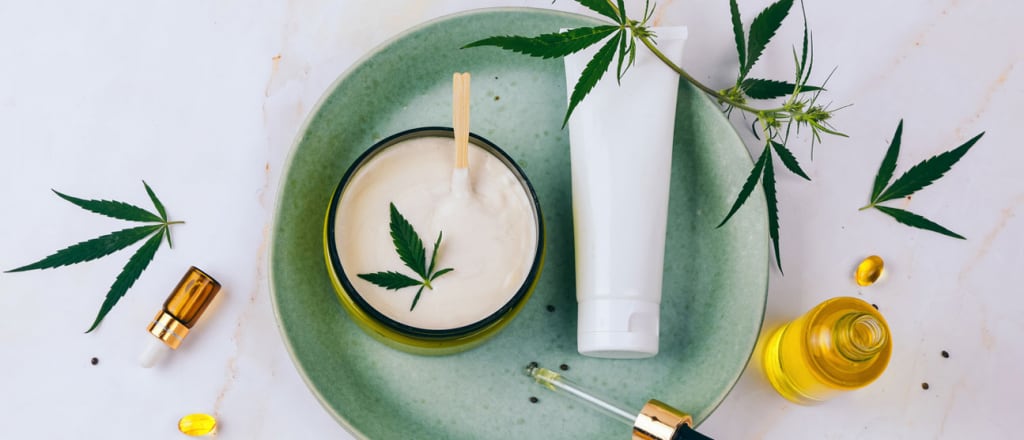 Cannabis-infused skincare creams and serums artfully assembled with cannabis leaves placed around them.