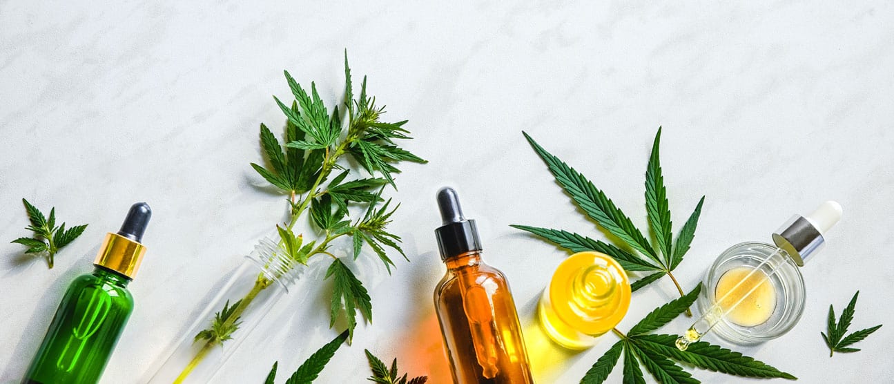 Assortment of CBD oil products in dropper bottles with hemp leaves arranged around them.